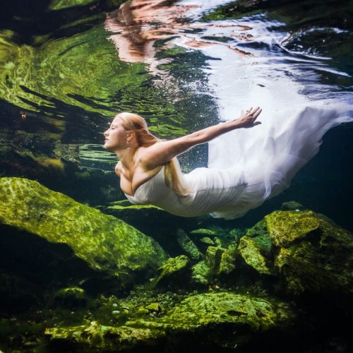 Bride swimming to surface in underwater trash the dress in Mayan Cenote at Riviera Maya