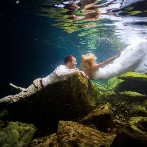 bride and Groom swimming towards each other in underwater trash the dress in Mayan Cenote at Riviera Maya