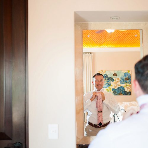 Groom looking in mirror getting ready for wedding.
