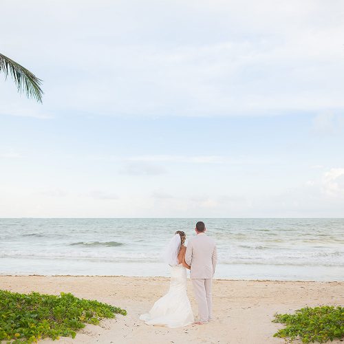 Bride and groom facing ocean under palm trees at NOW Jade Riviera Cancun wedding