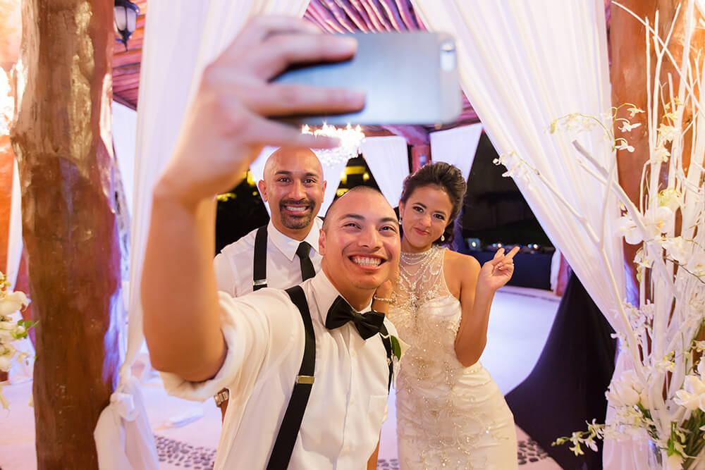 Bride and groom taking selfie with guest at wedding in Riviera Maya, Mexico