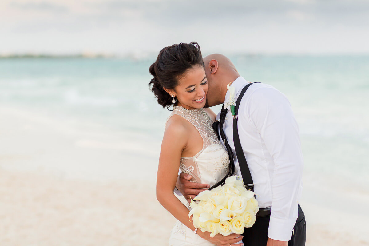 Groom kissing bride on beach at Secrets Maroma