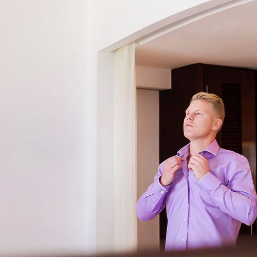 Groom buttoning up shirt before wedding