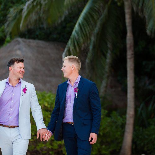 Grooms holding hands walking into reception at Live Aqua Cancun