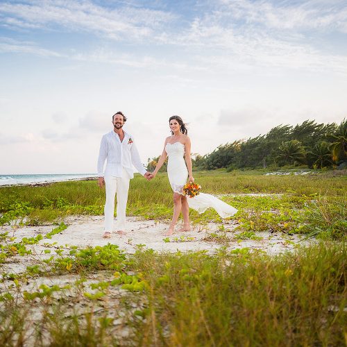 Portrait of Bride and groom in holding hands in grass near beach after wedding in Tulum
