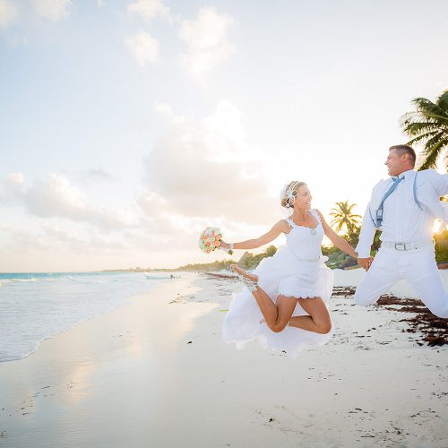 Bride and groom jumping on beach in Tulum