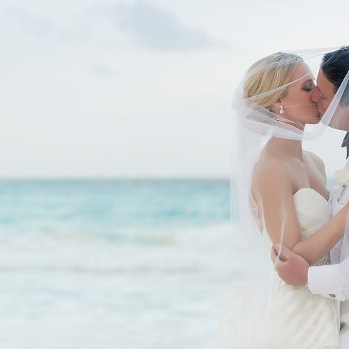 Couple under veil kissing a Hard Rock Cancun beach wedding