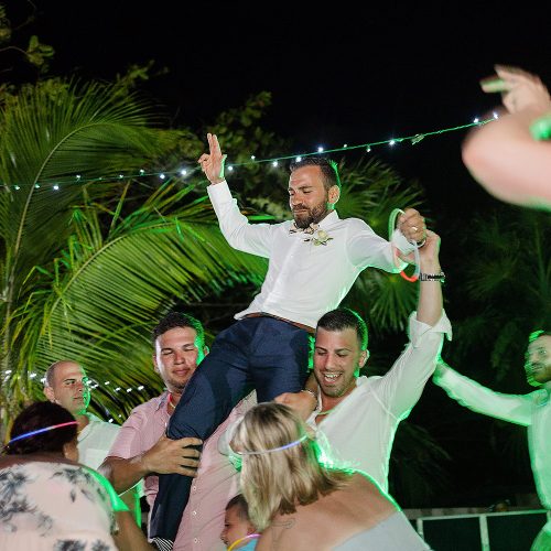 Groom being carried on shoulders of guests dancing at wedding reception
