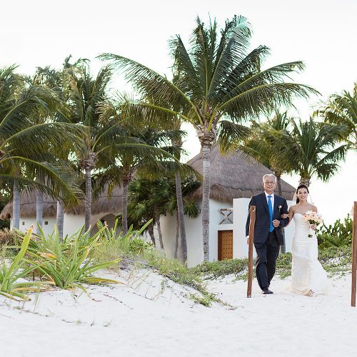 Bride walking with father to wedding reception on beach in Cancun