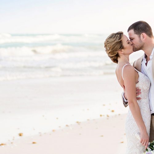 Groom kissing bride on beach in Tulum after wedding