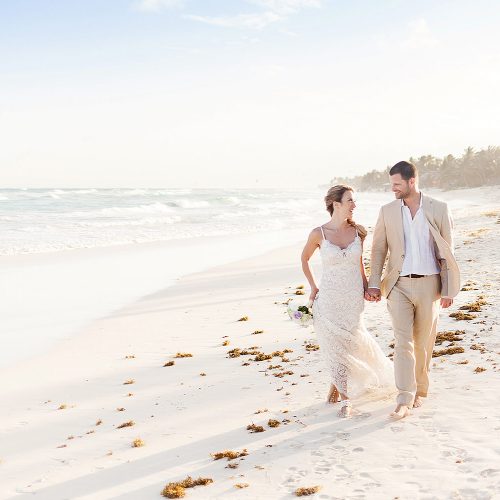 Bride and groom walking down beach in Tulum