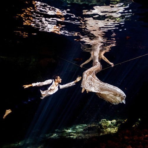 Groom reaching for his bride in underwater photography in Maya Cenote