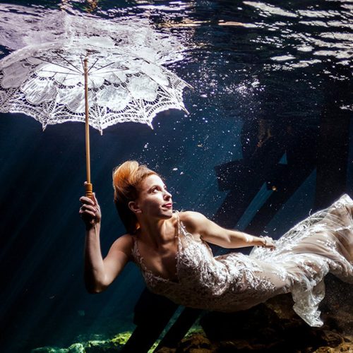 Bride holding an umbrella in underwater portrait in Maya Cenote