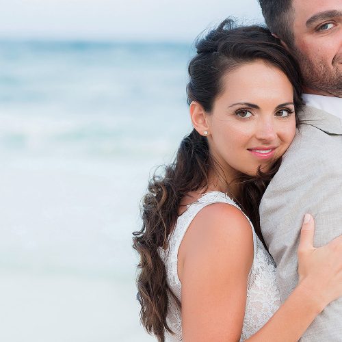 Bride hugging groom on beach.