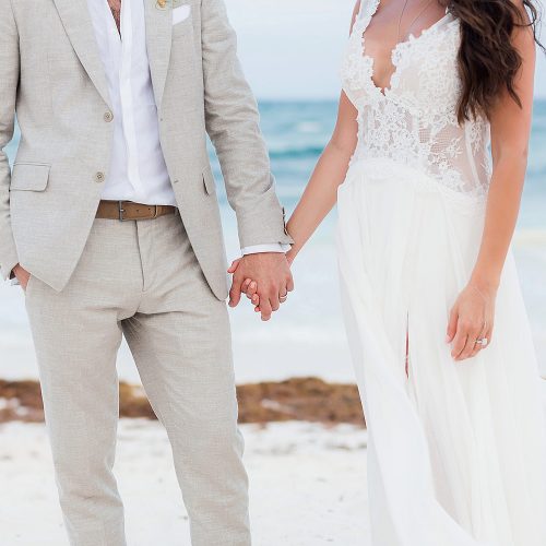 Close up of bride and groom holding hands on beach