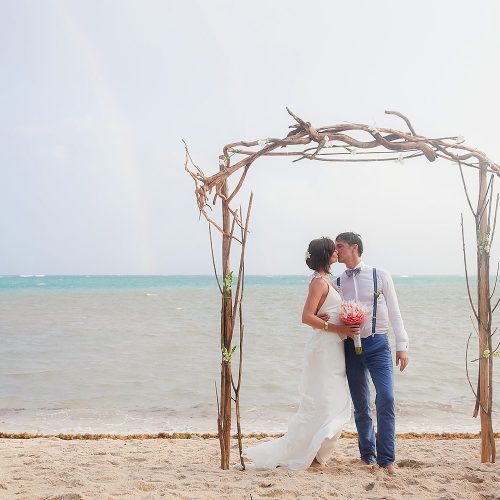 Bride and groom kissing under arch after a rainy ceremony in tulum