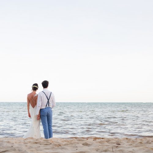 Bride and groom on beach looking at ocean in Tulum
