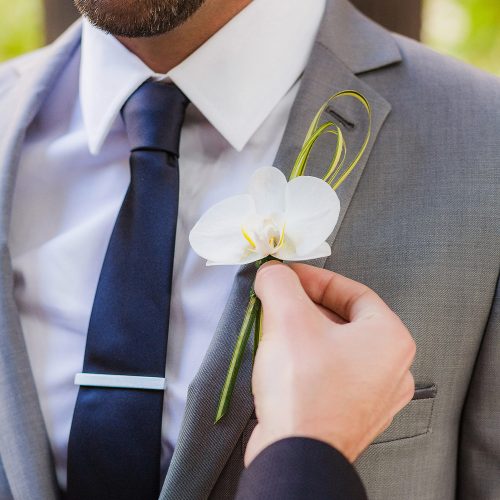 Close up of groom having boutonniere on at wedding