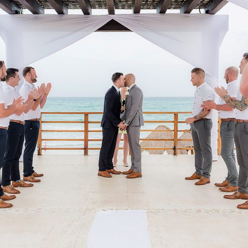 Grooms kissing at gay wedding under pergola at NOW Jade Riviera Cancun resort