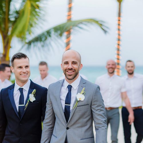Grooms walking with groomsmen behind in garden at NOW Jade Riviera Cancun