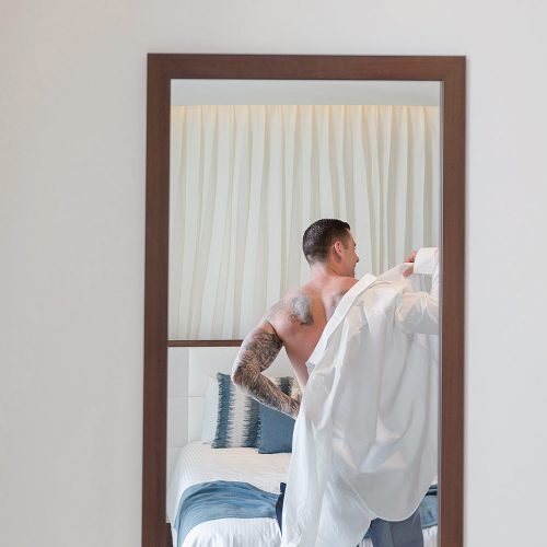 Groom putting on shirt in mirror at Secrets on the vine Cancun