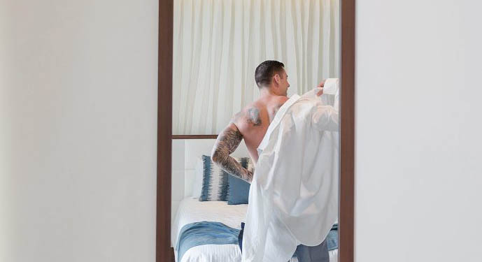 Groom putting on shirt in hotel room before wedding. 