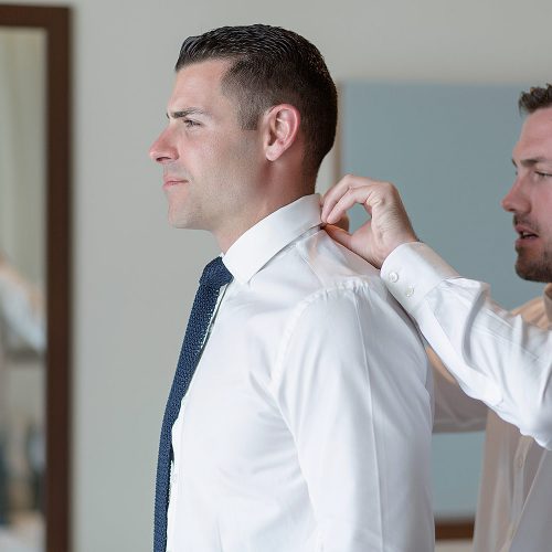 Best man helping groom with shirt collar