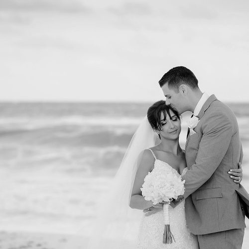 Groom kissing bride on head on beach in Cancun
