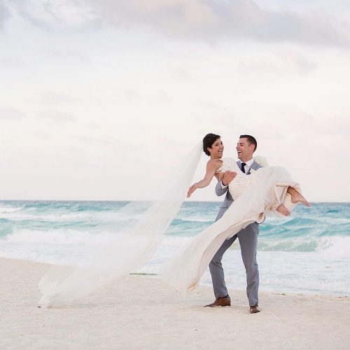 Groom carrying bride on beach in Cancun