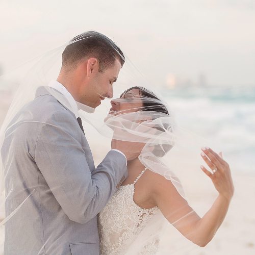 Bride and groom kissing under veil on beach in Cancun