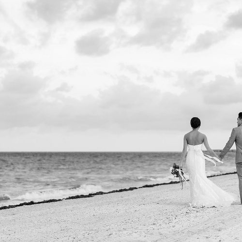 Bride and groom walking down beach holding hands in Cancun