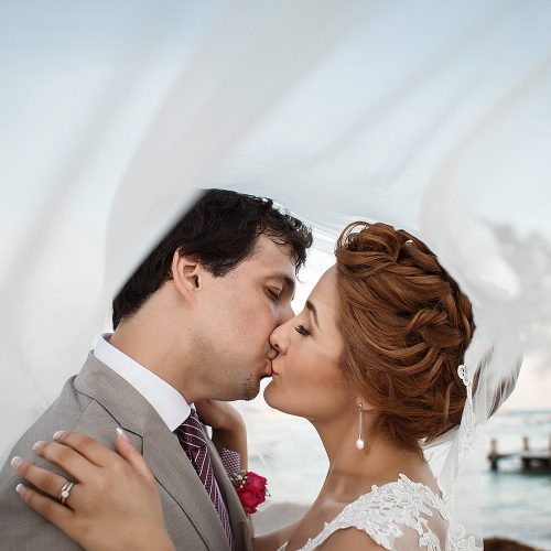 Bride and groom kissing under veil.