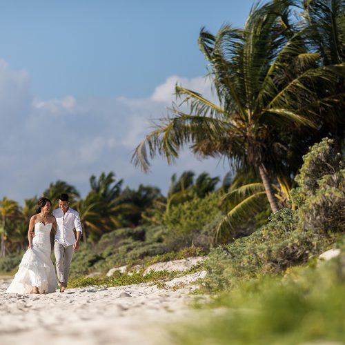 Bride and groom walking beside dune on beach in Riveira Maya Mexico