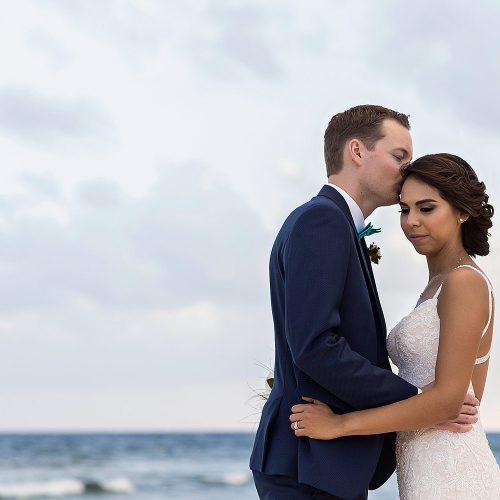 Groom kissing bride on forehead on beach in Riviera maya