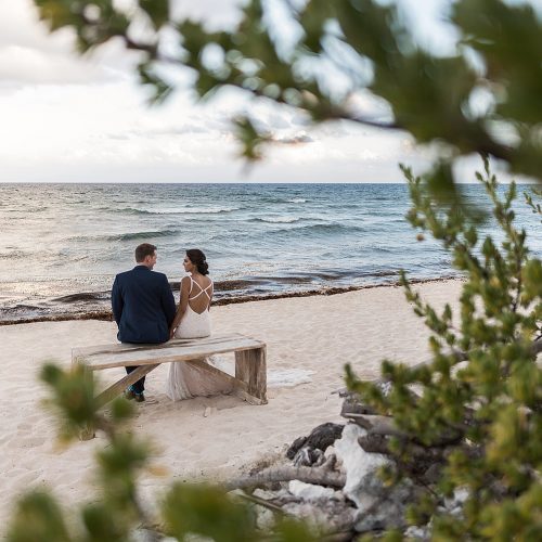Bride and groom sitting on bench looking at the sea