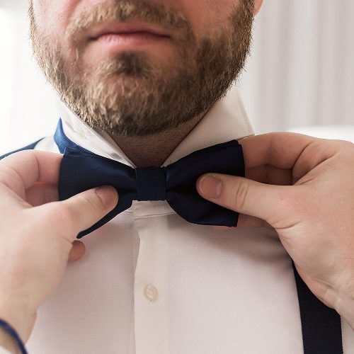 Close up of groom putting on bow tie