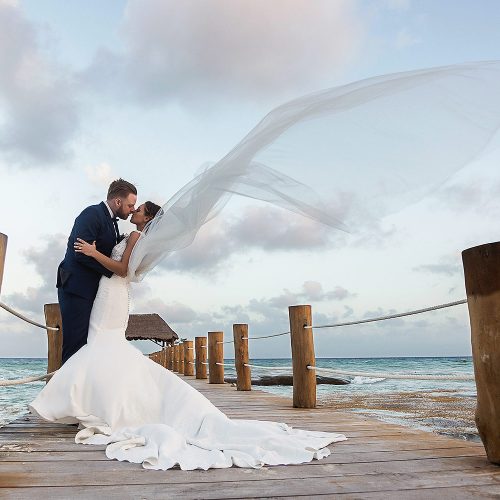 Bride and groom kissing with wind on dock at Azul Fives resort