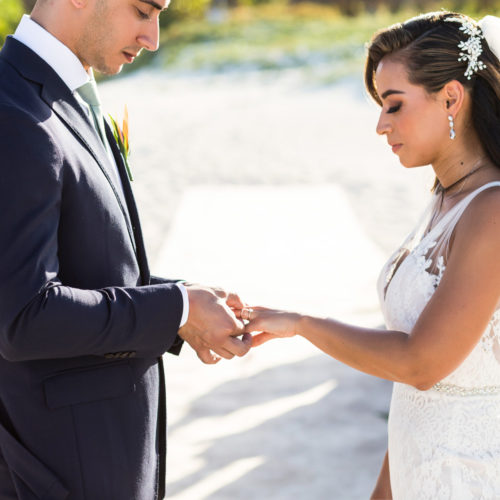 Bride and groom exchanging rings during beach wedding ceremony.