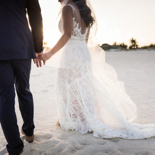 Bride and groom holding hands walking on beach.