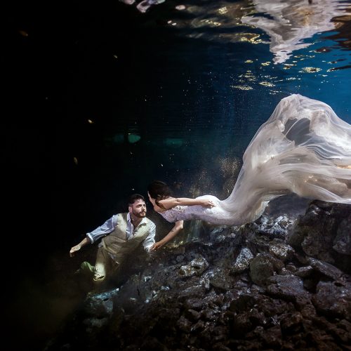 Bride swimming towards groom in mayan cenote TTD.
