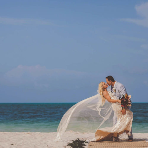 Bride and Groom kissing on beach with wind blowing veil at Finest Playa Mujeres