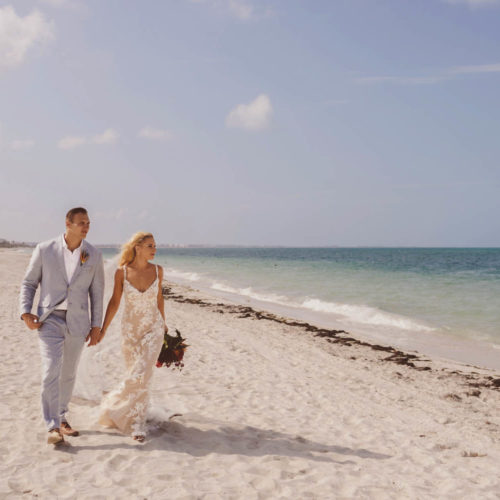 Wide angle photo of bride and groom walking on beach holding hands at Finest Playa Mujeres