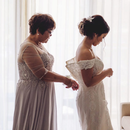 Mother helping bride get ready with window in background at Royalton Riviera Cancun