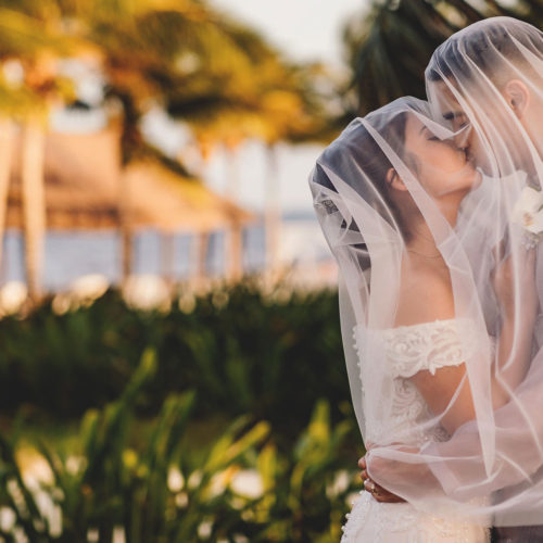 Bride and groom kissing under vaiel at Royalton Riviera Cancun